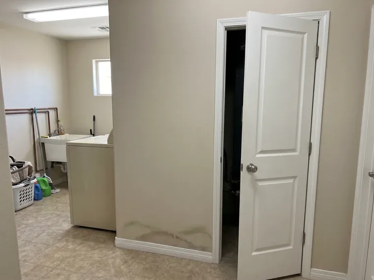 Interior of a Phoenix home utility area with an AC closet door ajar and faint water staining on the lower baseboard wall, mild early-stage moisture discoloration