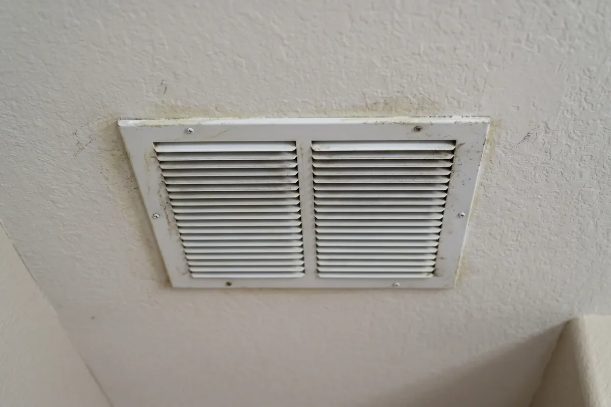 Ceiling AC supply vent in a Phoenix home with faint discoloration and dust around the edges, soft overhead light, residential interior.