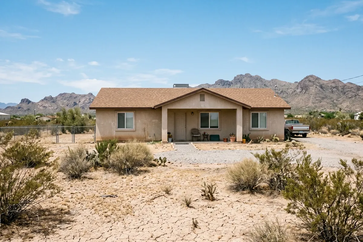 Dry Arizona desert landscape with cracked soil, sparse desert brush, and mountains in the background, hot midday sun, clear blue sky.