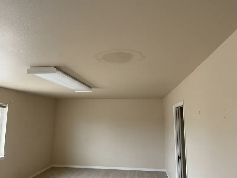 A faint brown water stain on the ceiling of an empty Phoenix room, beige paint, tide-mark rings showing the stain has been there a while, no furniture in the vacant space.