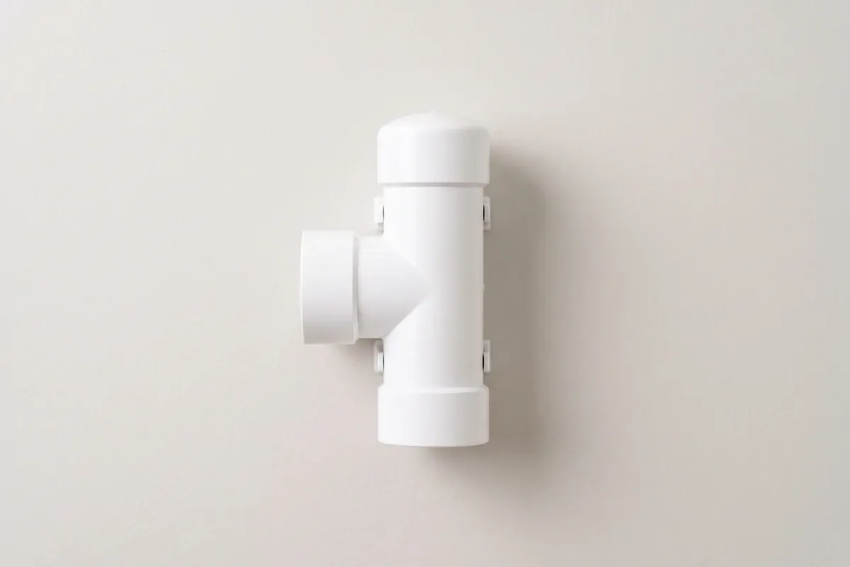 A simple white PVC condensate drain access tee near a home air handler, no gauges or readouts visible
