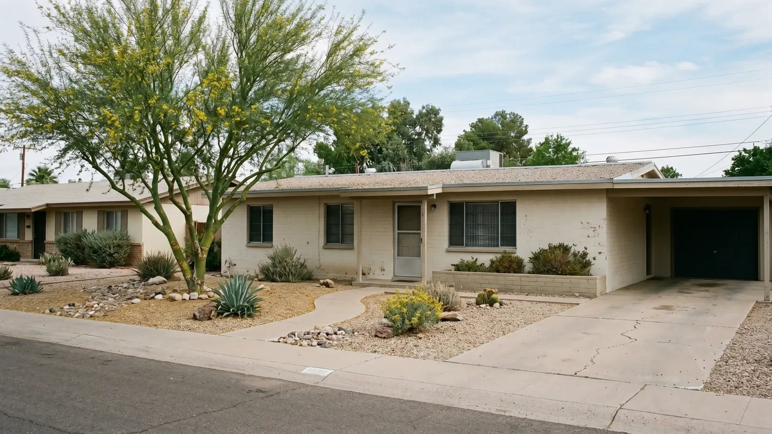 A single-story stucco ranch home from the 1960s on a quiet Phoenix street, mature desert landscaping, aged stucco, natural afternoon light.
