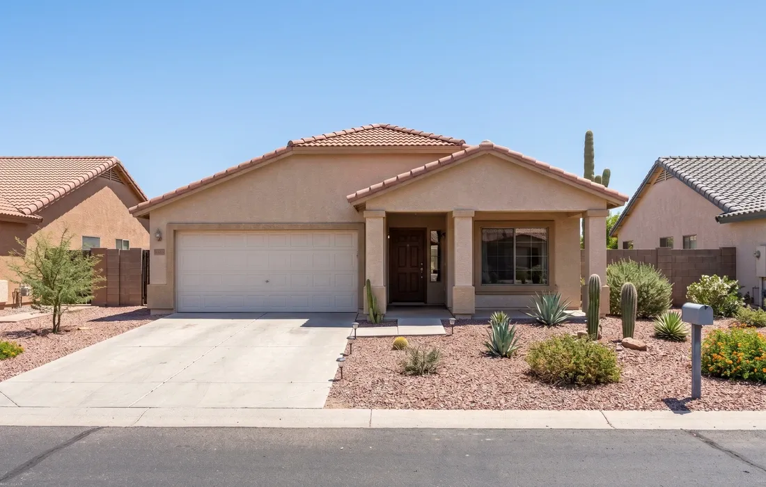 Single-story tan stucco Phoenix home with desert landscaping and terracotta tile roof, bright midday sun, clean exterior view
